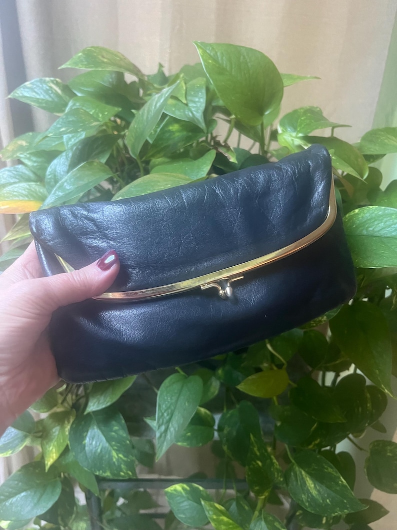 Pu&ograve; includere: Un portafoglio in pelle nera con una chiusura dorata. Il portafoglio &egrave; chiuso e ha un aspetto leggermente usurato.