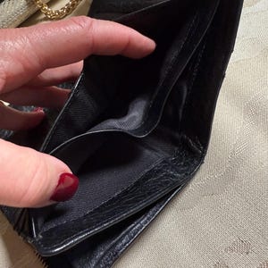 May include: Black leather wallet with a zipper closure and multiple compartments. The wallet is open and empty.