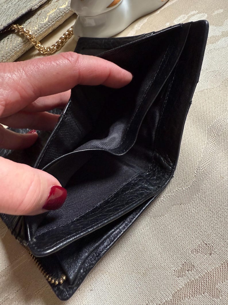 May include: Black leather wallet with a zipper closure and multiple compartments. The wallet is open and empty.
