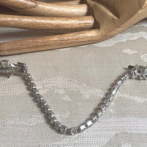 May include: A silver chain with two rhinestone-encrusted clips. The clips are shaped like crescent moons with a star design.