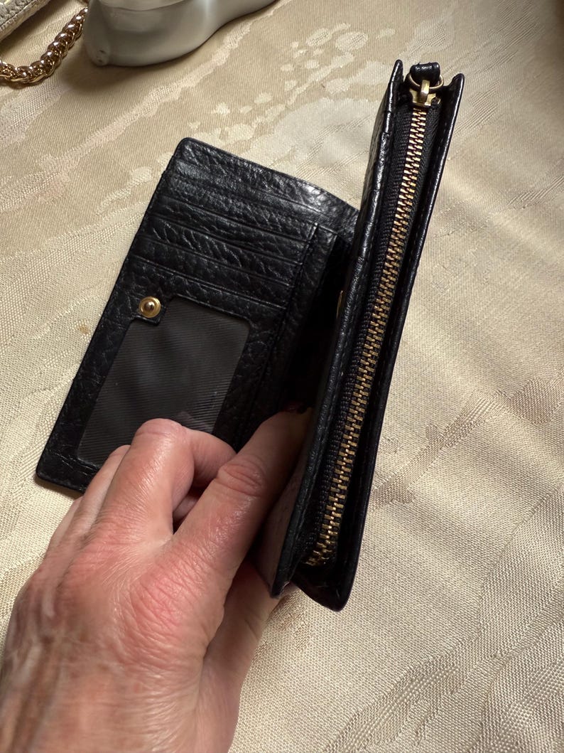 May include: Black leather wallet with a gold zipper and a clear plastic window for an ID card.