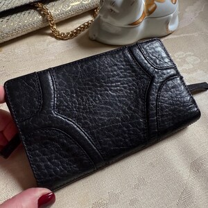 May include: Black leather wallet with a textured surface and a geometric design. The wallet has a zipper closure.