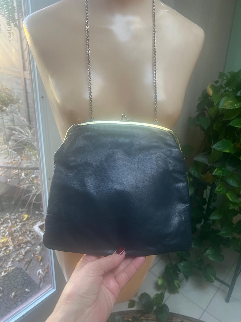 Pu&ograve; includere: Una pochette in pelle nera con una chiusura a scatto dorata e una tracolla a catena argentata.