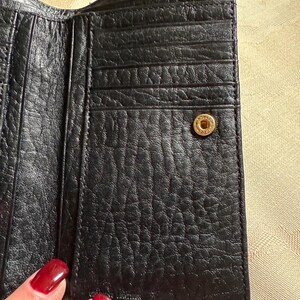 May include: Black leather wallet with multiple card slots and a snap closure. The wallet has a textured surface and a gold-colored button.