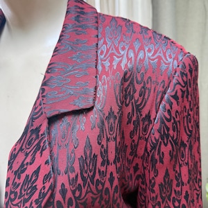 May include: A red blazer with a black damask pattern. The blazer has a collar and long sleeves.