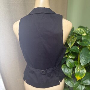 May include: Black vest with a collar and adjustable belt detail at the back. The vest is sleeveless and appears to be made of a woven fabric. The vest is displayed on a mannequin.
