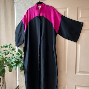 May include: A black and hot pink long-sleeved shirt dress with a mandarin collar and a button-up front. The dress has a split hem and a tassel detail at the collar.