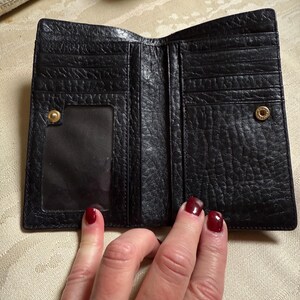 May include: Black leather wallet with multiple card slots and a clear ID window. The wallet is folded open to show the interior.