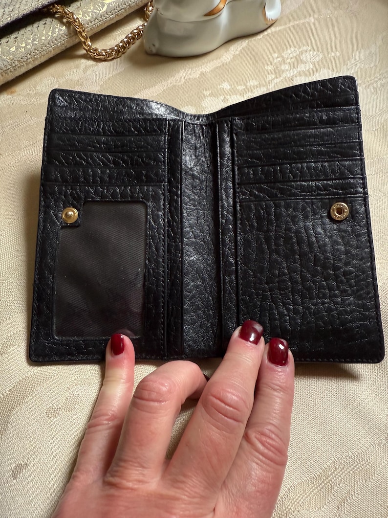 May include: Black leather wallet with multiple card slots and a clear ID window. The wallet is folded open to show the interior.