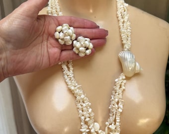May include: A multi-strand necklace made of small, irregular white shell chips featuring a large, smooth, iridescent white seashell accent. The set includes matching cluster earrings composed of small white shell beads arranged in a round shape.