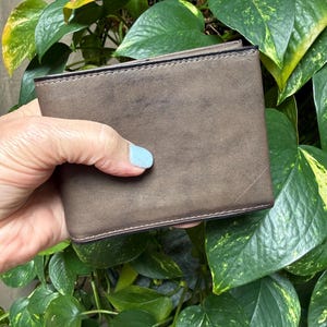 Può includere: Un portafoglio rettangolare pieghevole con finitura marrone opaco e cuciture sui bordi in marrone scuro. Il portafoglio presenta una superficie liscia e uniforme, con un design pulito e strutturato in un formato compatto.