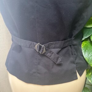 May include: Black vest with an adjustable belt and buckle. The vest is made of a smooth fabric and has a tailored fit. The buckle is silver-toned and adds a decorative element to the back of the vest.