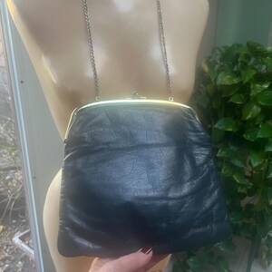 Pu&ograve; includere: Una pochette in pelle blu scuro con una chiusura dorata e una tracolla a catena argentata.