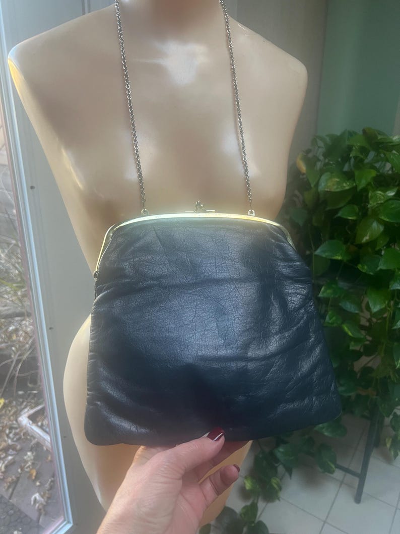 Pu&ograve; includere: Una pochette in pelle blu scuro con una chiusura dorata e una tracolla a catena argentata.