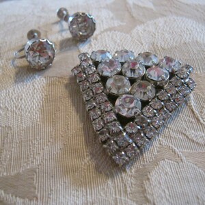 Pu&ograve; includere: Un set di gioielli vintage con una spilla triangolare con strass trasparenti e un paio di orecchini abbinati con pietre trasparenti.