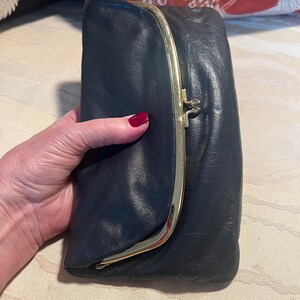 Pu&ograve; includere: Una pochette in pelle blu scuro con una chiusura a scatto dorata.