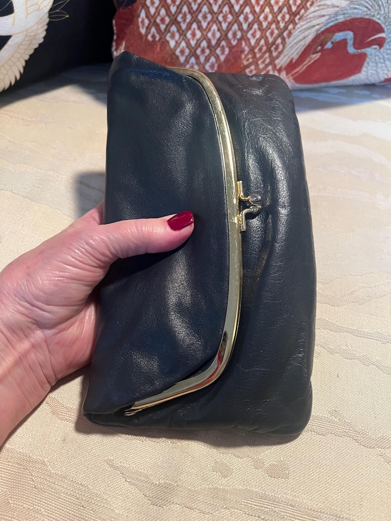 Pu&ograve; includere: Una pochette in pelle blu scuro con una chiusura a scatto dorata.