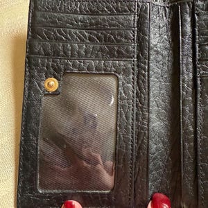 May include: Black leather trifold wallet with a clear plastic ID window and a gold-toned button closure.