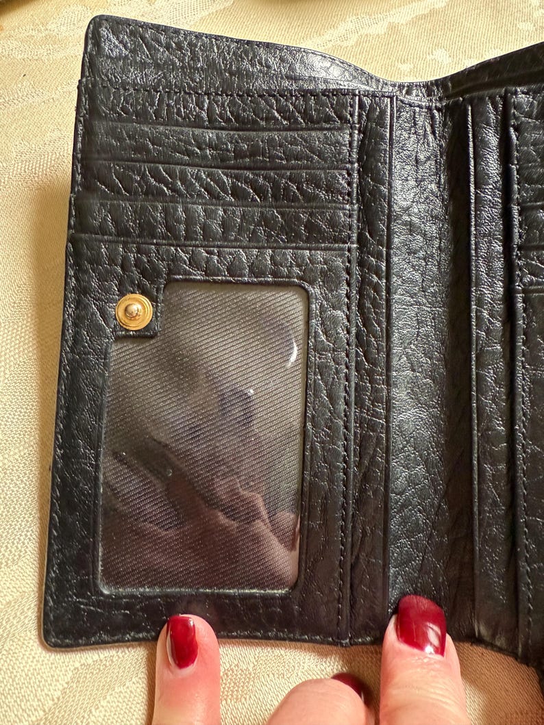 May include: Black leather trifold wallet with a clear plastic ID window and a gold-toned button closure.