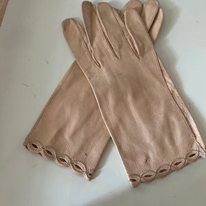 May include: A pair of light beige leather gloves with a scalloped edge. The gloves are made of a soft, supple leather and have a classic design.