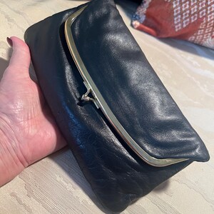 Pu&ograve; includere: Una pochette in pelle nera con una chiusura a scatto dorata.
