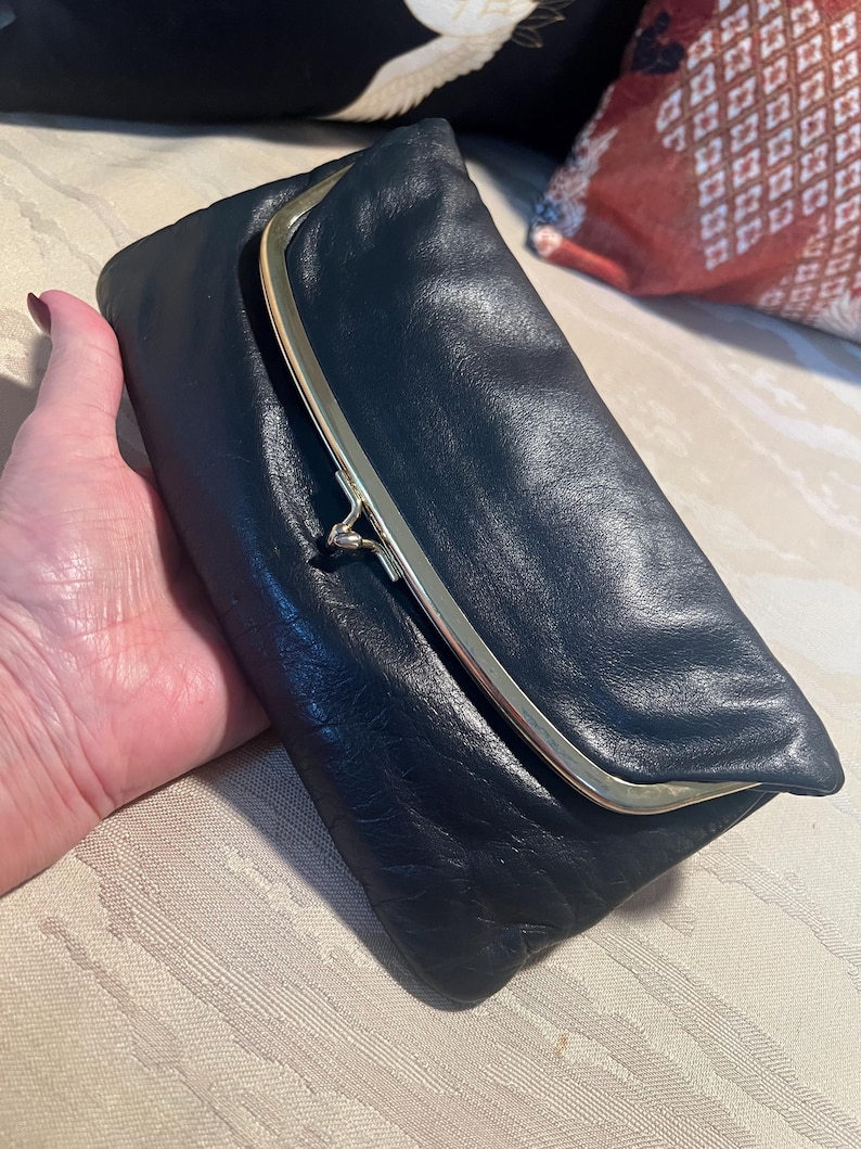 Pu&ograve; includere: Una pochette in pelle nera con una chiusura a scatto dorata.