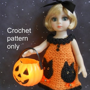 May include: A crocheted Halloween costume for a doll, featuring an orange dress with black cat appliques and a black crocheted collar. The doll is holding a pumpkin-shaped trick-or-treat bucket.