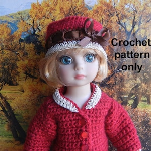 Może przedstawiać: Czerwony kardigan na szydełku z białymi lamówkami i czerwonymi guzikami. Kardigan nosi lalka z blond włosami i czerwonym kapeluszem na szydełku z brązową wstążką i białymi lamówkami. Lalka stoi przed rozmytym tłem jesiennych liści.