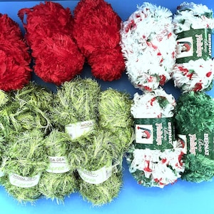 May include: An assortment of colorful yarn skeins in red, green, and white. The red yarn is a fluffy texture, while the green yarn is labeled "MODA DEA Spree". Some skeins are labeled "Bernat Boa Holidays" with a festive design.