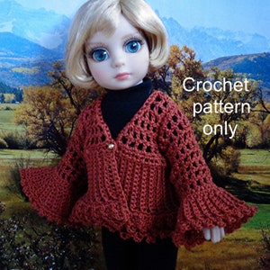 May include: Crochet pattern only. A doll wearing a red crocheted cardigan with bell sleeves. The cardigan has a button closure and a lacy design.