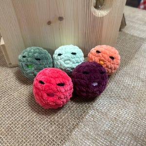 Peut inclure: Cinq petites boules en crochet avec des visages brodés. Les boules sont de différentes couleurs, notamment le vert, le rose, le violet et l'orange.