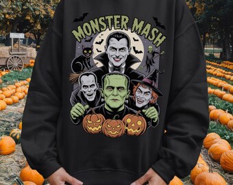 May include: Black sweatshirt featuring a Halloween-themed graphic with the text "Monster Mash." The design includes classic monster characters like Dracula, Frankenstein, and a witch, along with bats and pumpkins. The sweatshirt is a crew neck style.