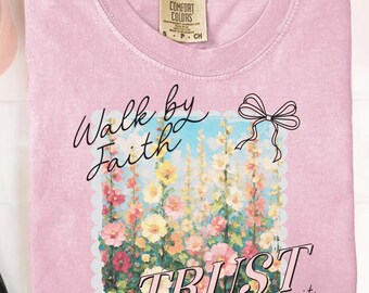 May include: A pale pink Comfort Colors t-shirt with the word "BLOSSOM" in a pink circle at the top. The shirt features a floral design with the words "Walk by Faith TRUST even when you can't see it."