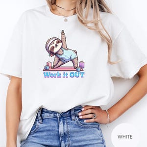 Könnte beinhalten: Weißes T-Shirt mit einem Cartoon-Faultier, das Yoga macht. Das Faultier trägt ein Stirnband und einen hellblauen Body. Der Text "Work it OUT" ist darunter in Blau und Rosa gedruckt. Das Shirt ist ein lässiger Stil.