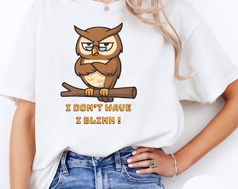 Puede incluir: Camiseta blanca con un diseño de búho de dibujos animados. El búho, con los brazos cruzados y gafas, está posado en una rama. El texto de abajo dice "I DON'T WAVE I BLINK!".
