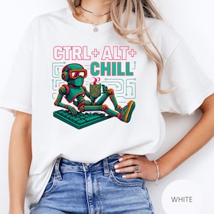 Puede incluir: Camiseta blanca con un gráfico colorido de un robot relajándose en un teclado, sosteniendo una taza. El texto "CTRL + ALT + CHILL" está encima del robot. El robot es de color verde azulado, naranja y negro.
