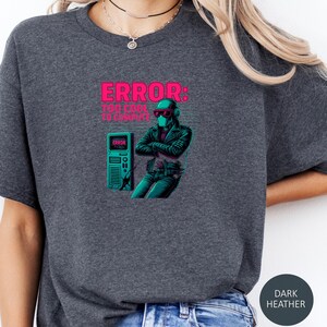May include: Dark heather gray t-shirt with a graphic that reads "ERROR: TOO COOL TO COMPUTE." The design features a futuristic figure in a leather jacket and sunglasses, with a computer tower. The shirt is a comfortable, casual wear.