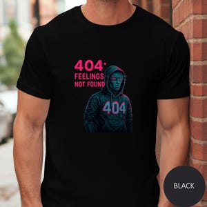May include: Black t-shirt featuring a digital art design. The design includes the text "404 FEELINGS NOT FOUND" in pink, along with a hooded figure with digital-style eyes and the number "404" on the hoodie. A black circle with the word "BLACK" is at the bottom.