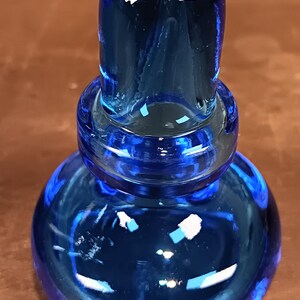 May include: A vibrant blue glass bottle stopper. The stopper has a rounded base, a ringed midsection, and a cylindrical top. The glass reflects light, creating highlights and shadows. The object is likely for wine bottles.