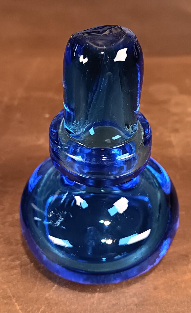 May include: A vibrant blue glass bottle stopper. The stopper has a rounded base, a ringed midsection, and a cylindrical top. The glass reflects light, creating highlights and shadows. The object is likely for wine bottles.