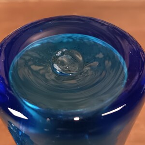 May include: A close-up view of a blue glass vase with a unique, swirling interior design. The vase features a deep blue exterior that transitions to a lighter turquoise hue inside, creating a captivating visual effect. The glass appears smooth and reflective.