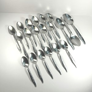May include: A collection of stainless steel spoons with a floral design on the handles. The spoons are arranged on a white surface, reflecting light. The spoons are a common kitchen utensil.