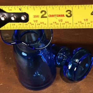 May include: A cobalt blue glass creamer with a flared spout and handle. The creamer is approximately 3 inches tall, as measured by a yellow Craftsman tape measure.