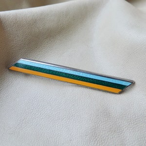 Könnte beinhalten: Eine silberfarbene Bar-Brosche mit einem blauen, grünen und gelben Emaille-Design.
