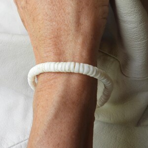 May include: A white bracelet made of small, rounded beads. The bracelet is worn on a wrist, and the beads are strung together to form a circular shape. The bracelet is a simple, elegant piece of jewelry.