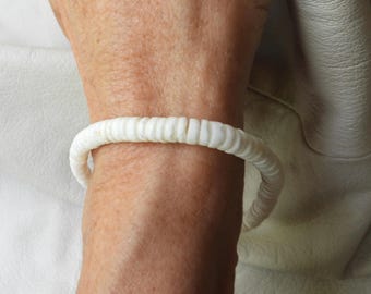 Könnte beinhalten: Ein weißes Armband aus kleinen, abgerundeten Perlen. Das Armband wird am Handgelenk getragen, und die Perlen sind zu einer kreisförmigen Form aufgereiht. Das Armband ist ein schlichtes, elegantes Schmuckstück.