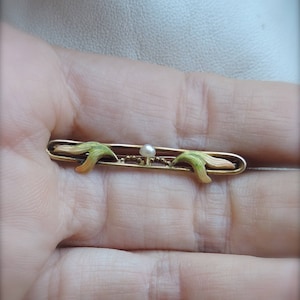 May include: A gold bar pin with a pearl in the center and green and pink enamel accents.