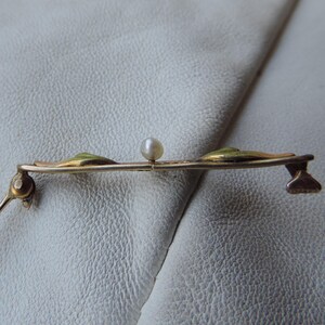 May include: A gold-toned brooch with three green enamel leaves and a single white pearl in the center.