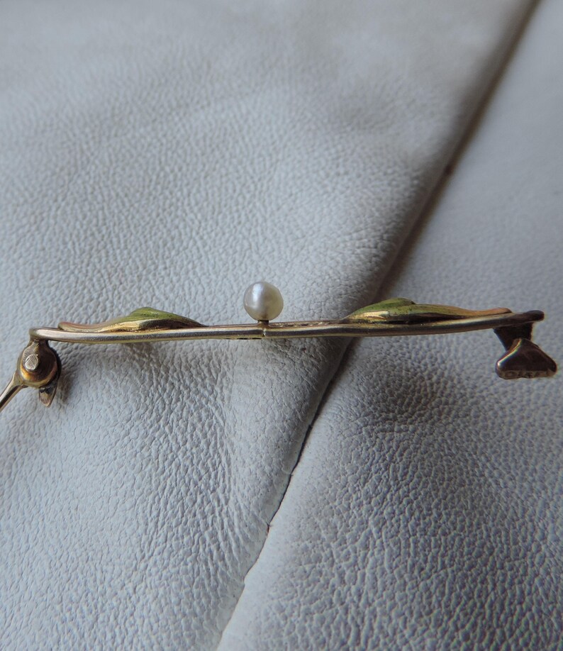 May include: A gold-toned brooch with three green enamel leaves and a single white pearl in the center.