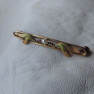 May include: A gold-toned brooch with a pearl in the center and green enamel leaves on either side.
